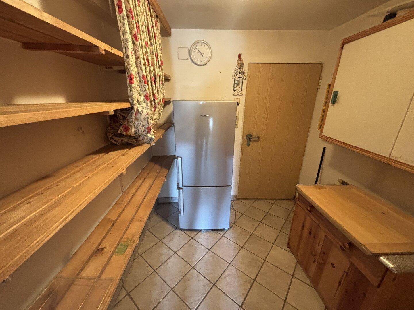 Praktischer Vorratsraum mit Regalen, Kühlschrank und Fliesenboden.