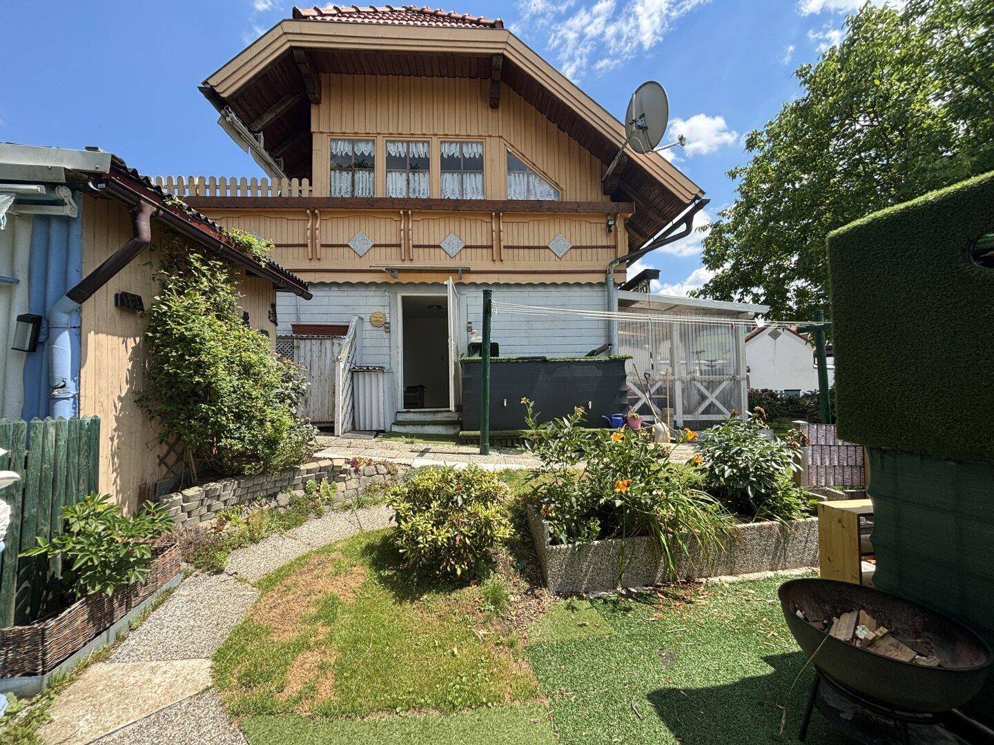 Hinterhof mit Rasenfläche, Hochbeeten und einem Grillbereich unter blauem Himmel.