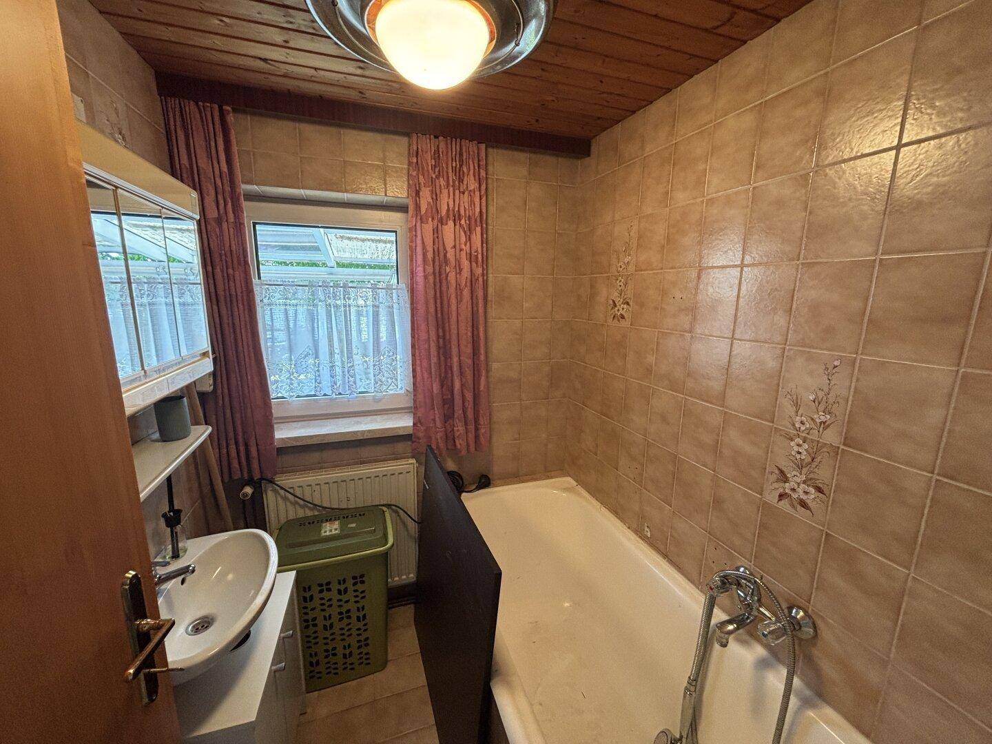Badezimmer mit Badewanne, Waschbecken und braunen Fliesen im 80er-Jahre-Stil.