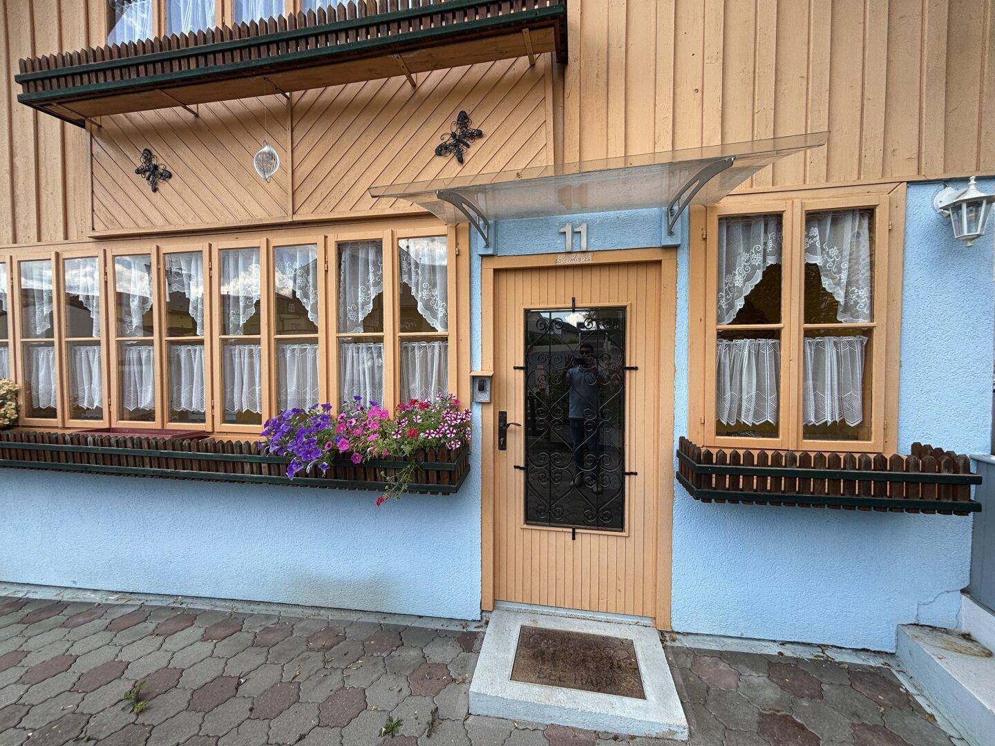 Eingangsbereich des Hauses mit Holztür, Blumenkästen und einem kleinen Vordach.