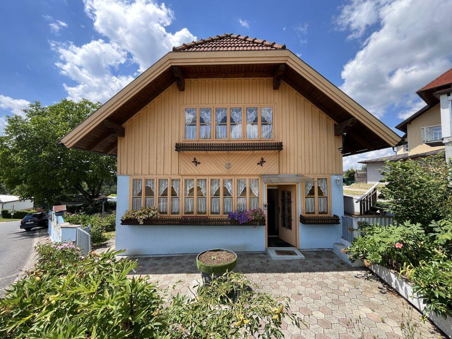 Charmantes Holzhaus mit blauer Fassade, Satteldach und gepflastertem Vorgarten unter blauem Himmel.