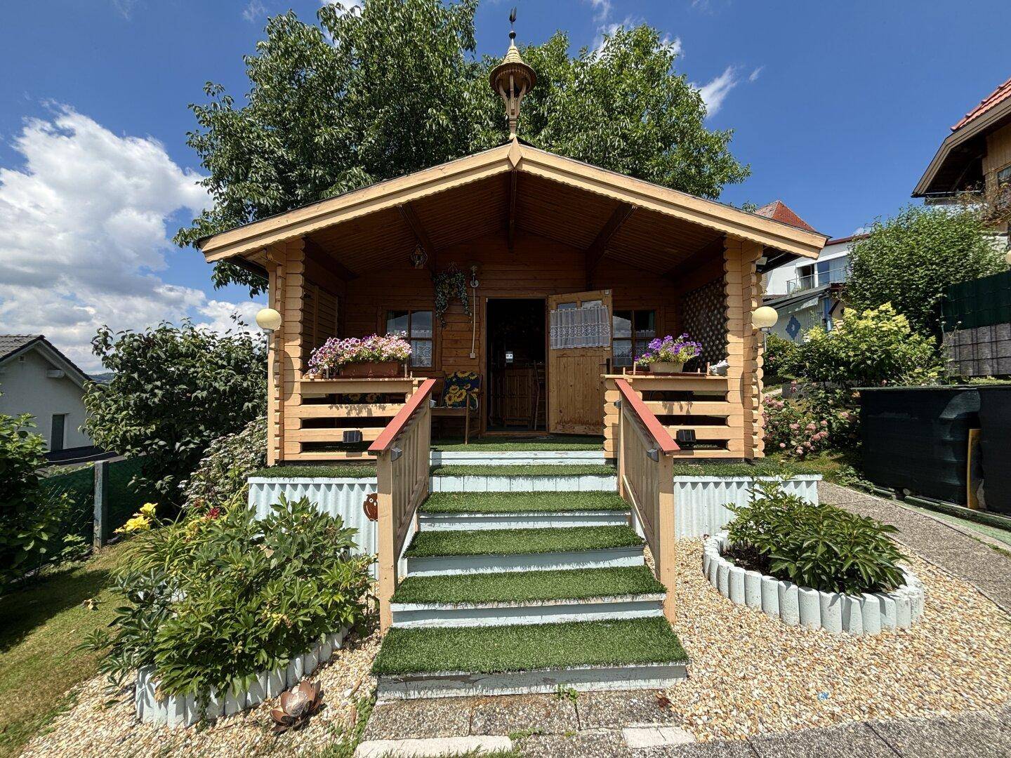 Charmantes Holzgartenhaus mit Treppe und Blumenkästen, umgeben von Grün.