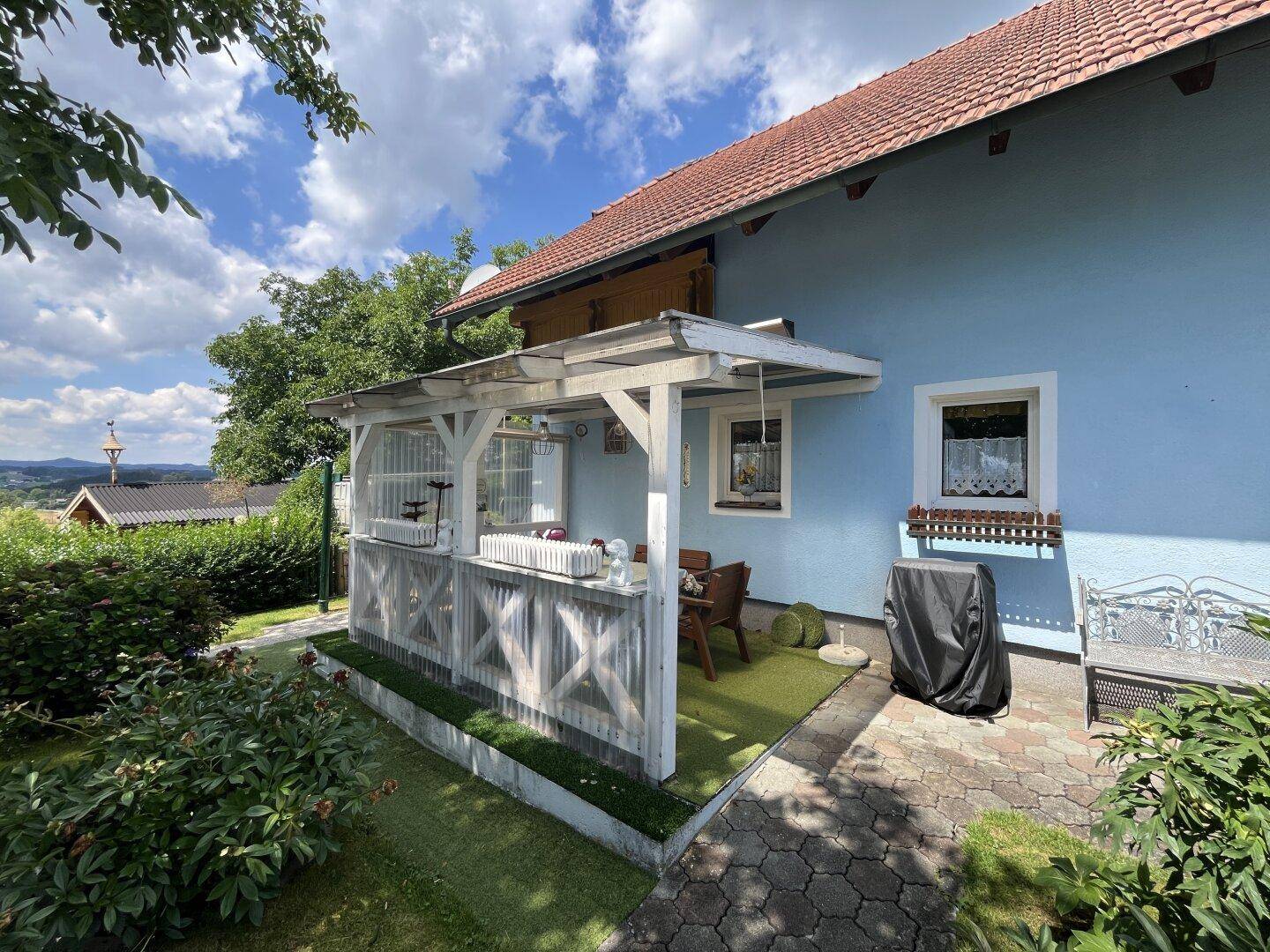 Überdachte Terrasse mit Gartenmöbeln am blauen Haus, ideal für entspannte Stunden.