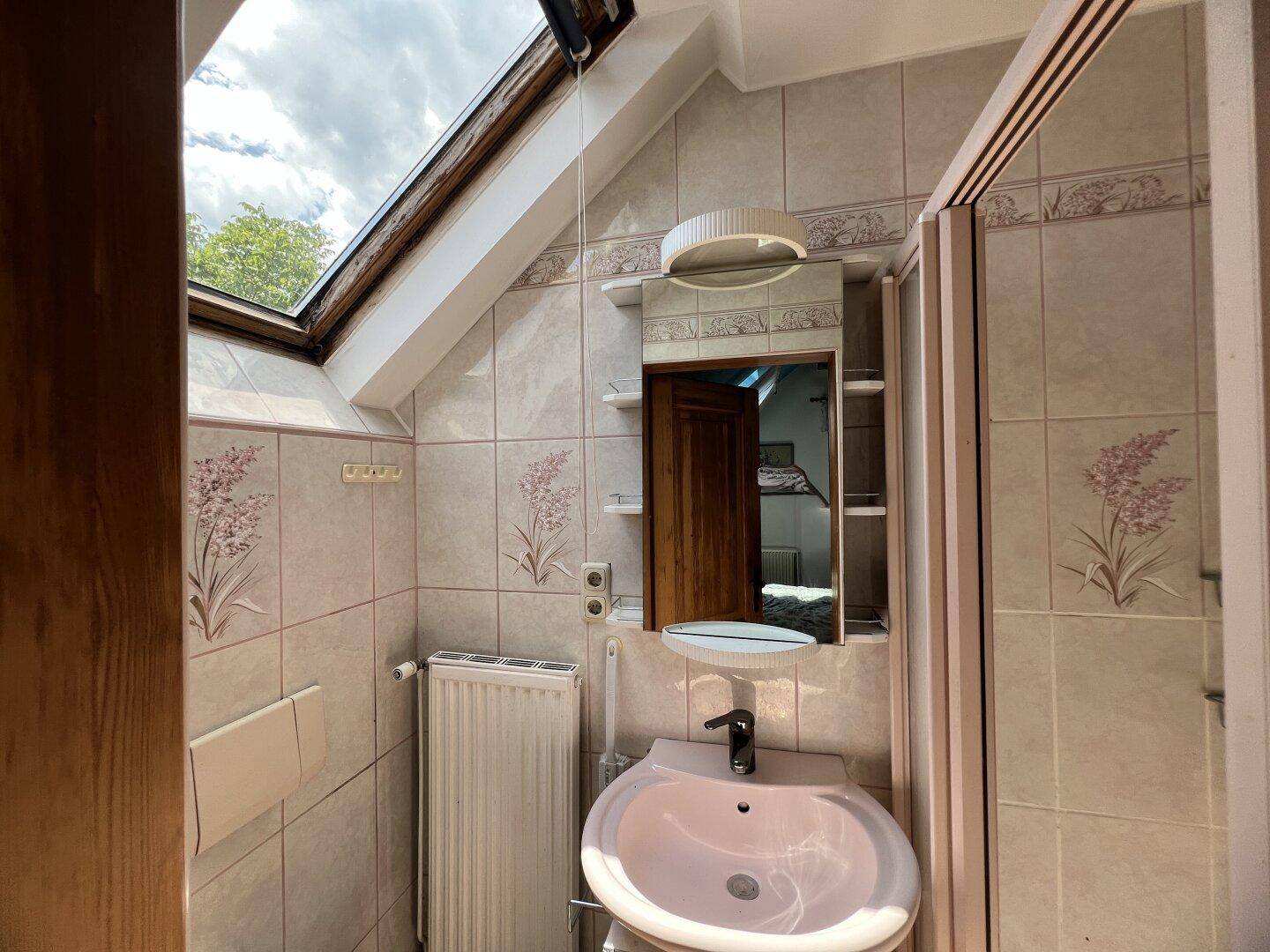 Badezimmer im Dachgeschoss mit Dachfenster, Waschbecken und Duschkabine.