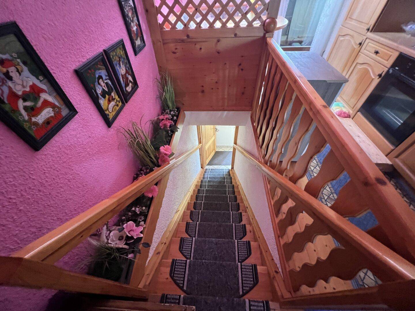 Holztreppe mit Teppichläufern und pinkfarbener Wandgestaltung.