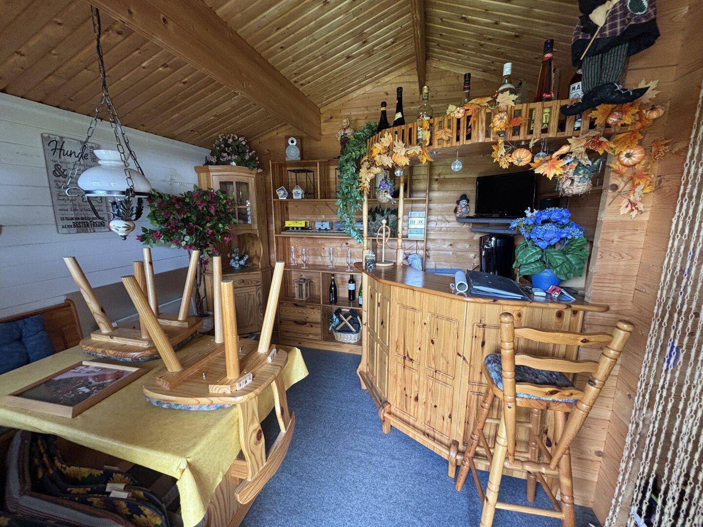 Gemütlicher Innenraum des Gartenhauses mit Holzvertäfelung, Bar und rustikalen Möbeln.