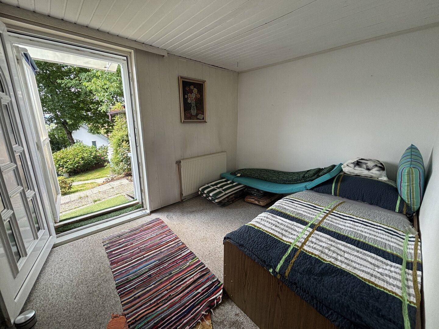 Einfaches Schlafzimmer mit Teppichboden und direktem Zugang zum Garten.