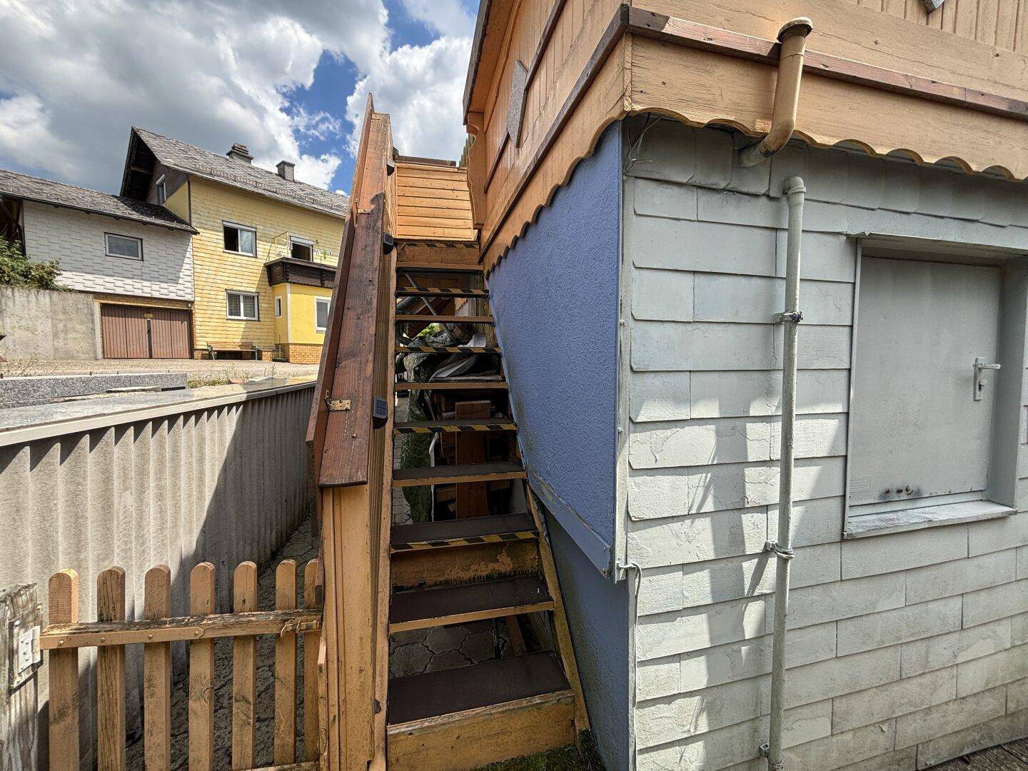 Hölzerne Außentreppe führt zu einem Gebäude mit blauer Fassade und Schindeln.