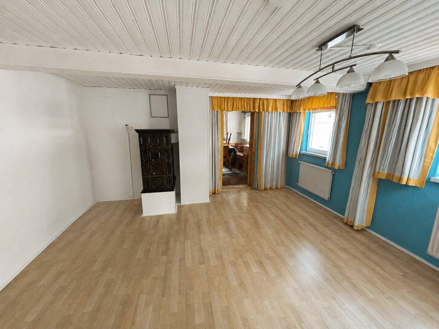 Geräumiges Wohnzimmer mit hellem Laminatboden, Kachelofen und blauen Akzentwänden.