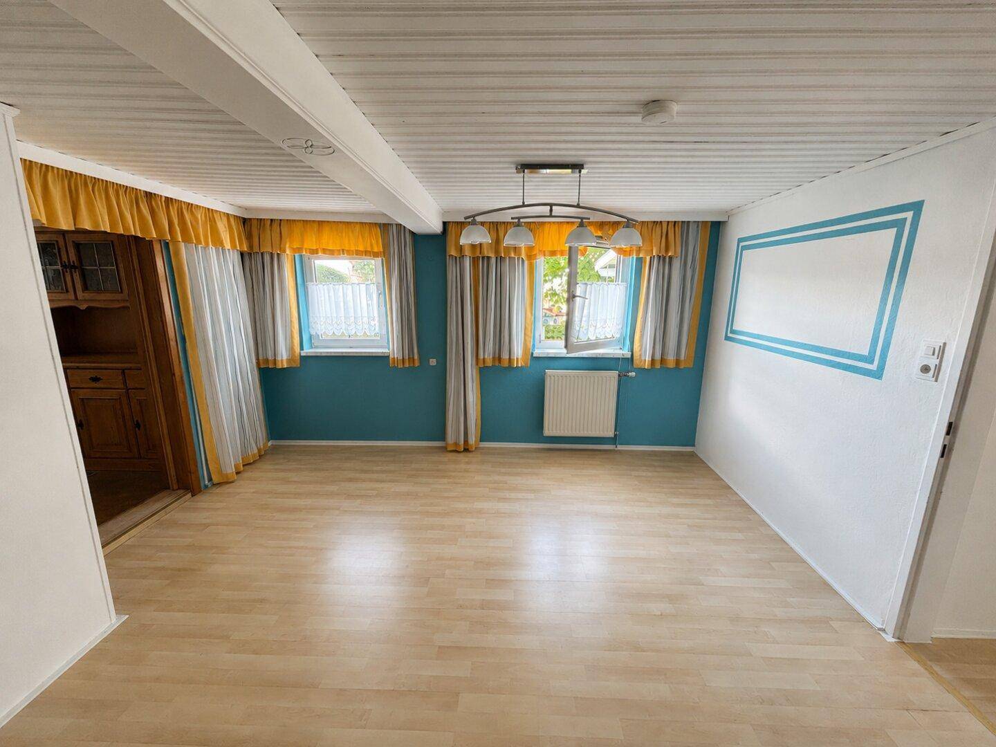 Helles Wohnzimmer mit Laminatboden, blauen Wänden und traditionellen Vorhängen.