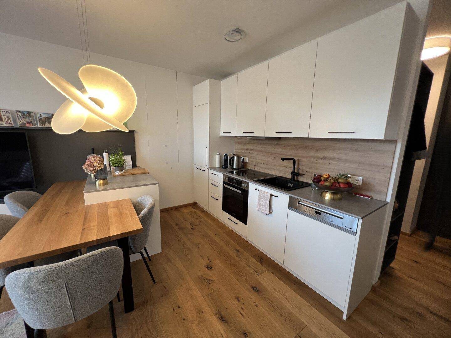 Helle, moderne Küche mit weißen Schränken, Holzakzenten und Essbereich.