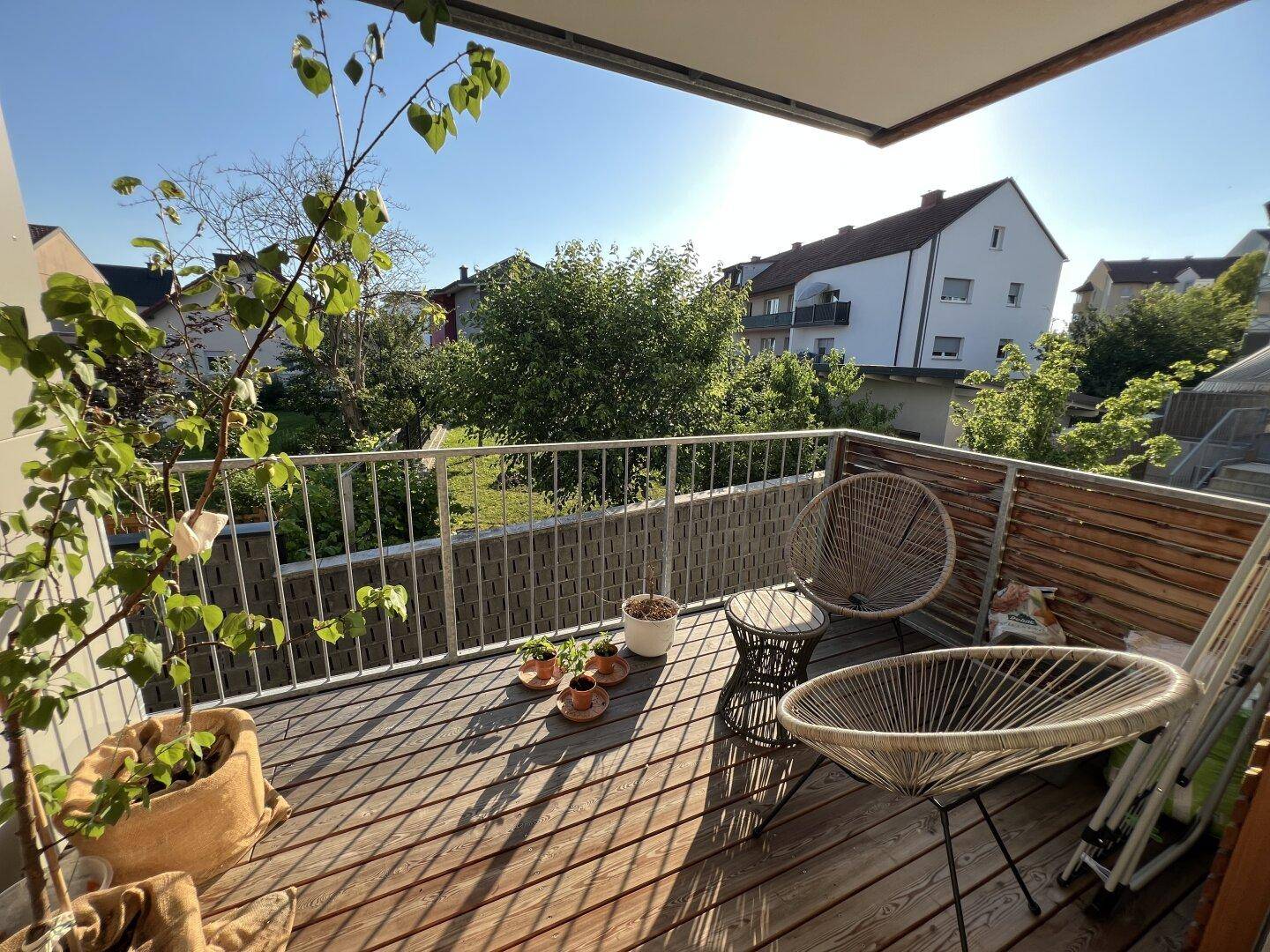 Sonniger Balkon mit Holzbelag, gemütlichen Sitzgelegenheiten und Blick ins Grüne.