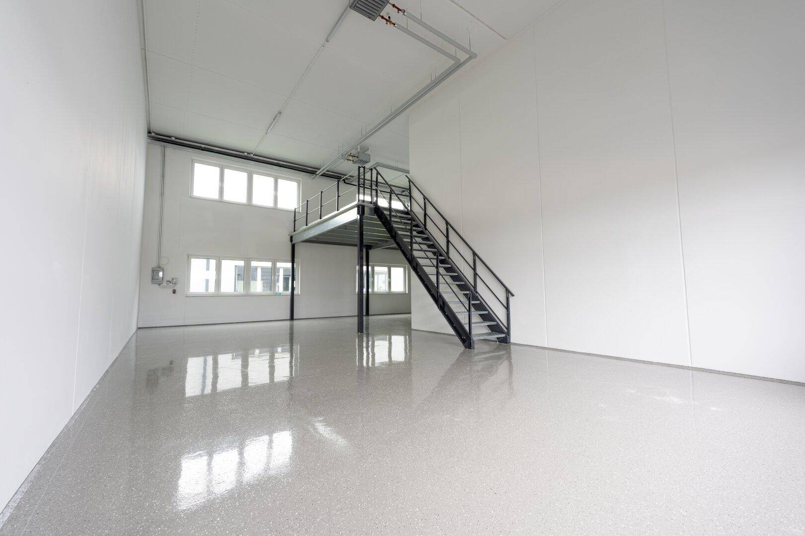 Heller, offener Gewerberaum mit glänzendem Industrieboden und einer Metalltreppe zur Empore.