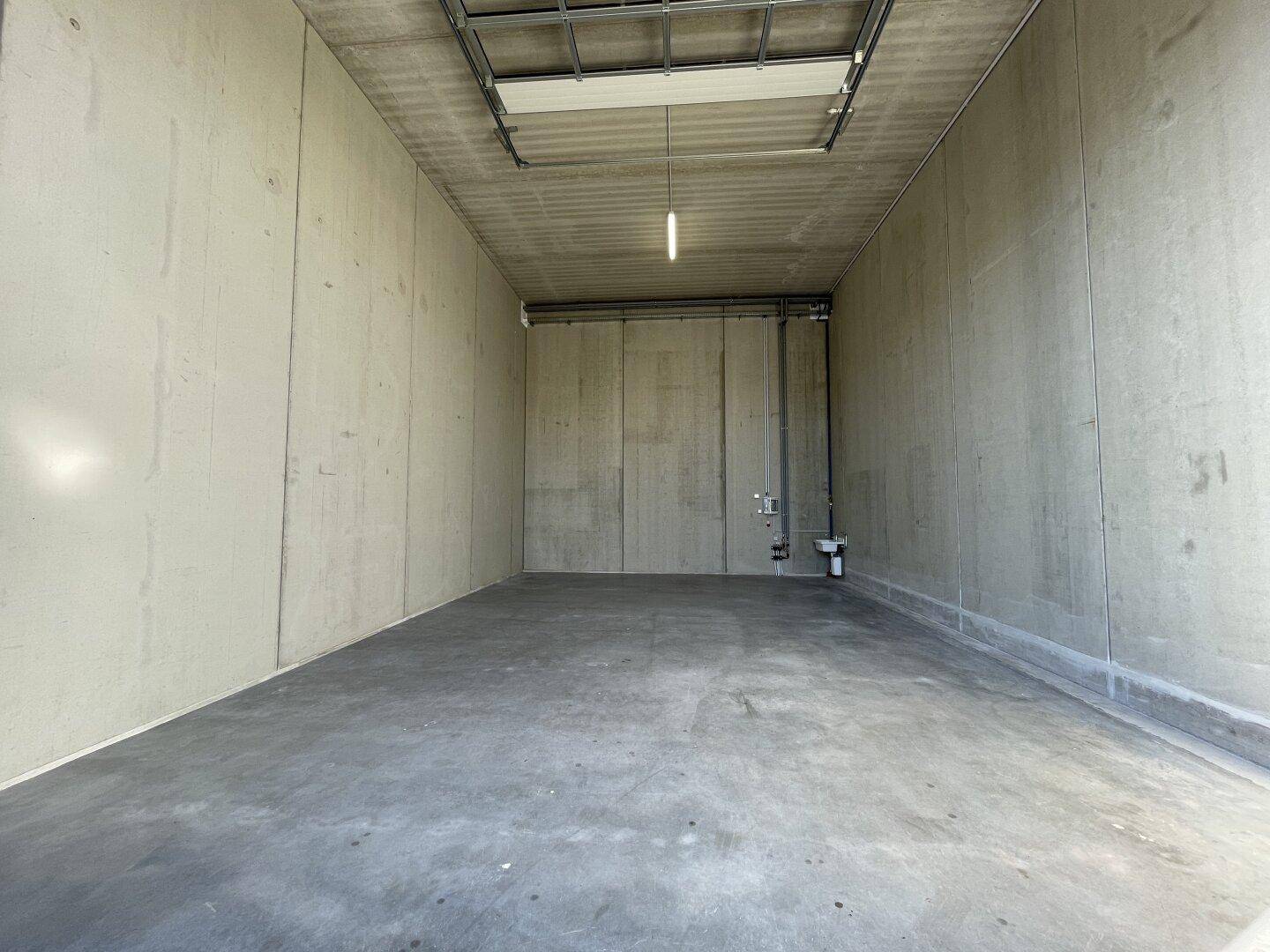Geräumiger, leerer Lagerraum mit Betonwänden, Industrieboden und einfacher Deckenbeleuchtung.