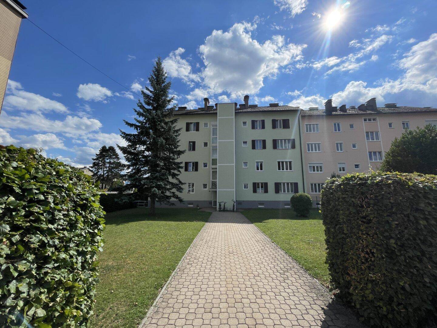 Wohngebäude mit gepflegter Grünfläche und einem gepflasterten Weg unter strahlendem Himmel.