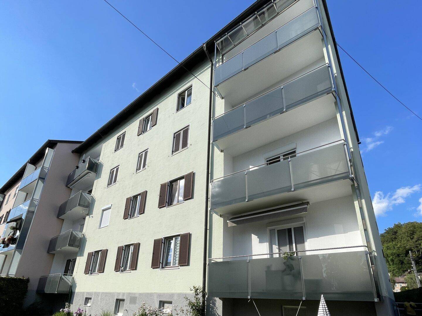 Fassade eines Mehrfamilienhauses mit mehreren Balkonen und braunen Fensterläden.