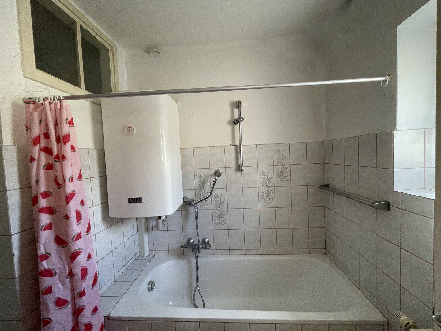 Badezimmer mit Badewanne, Boiler und älteren Fliesen.