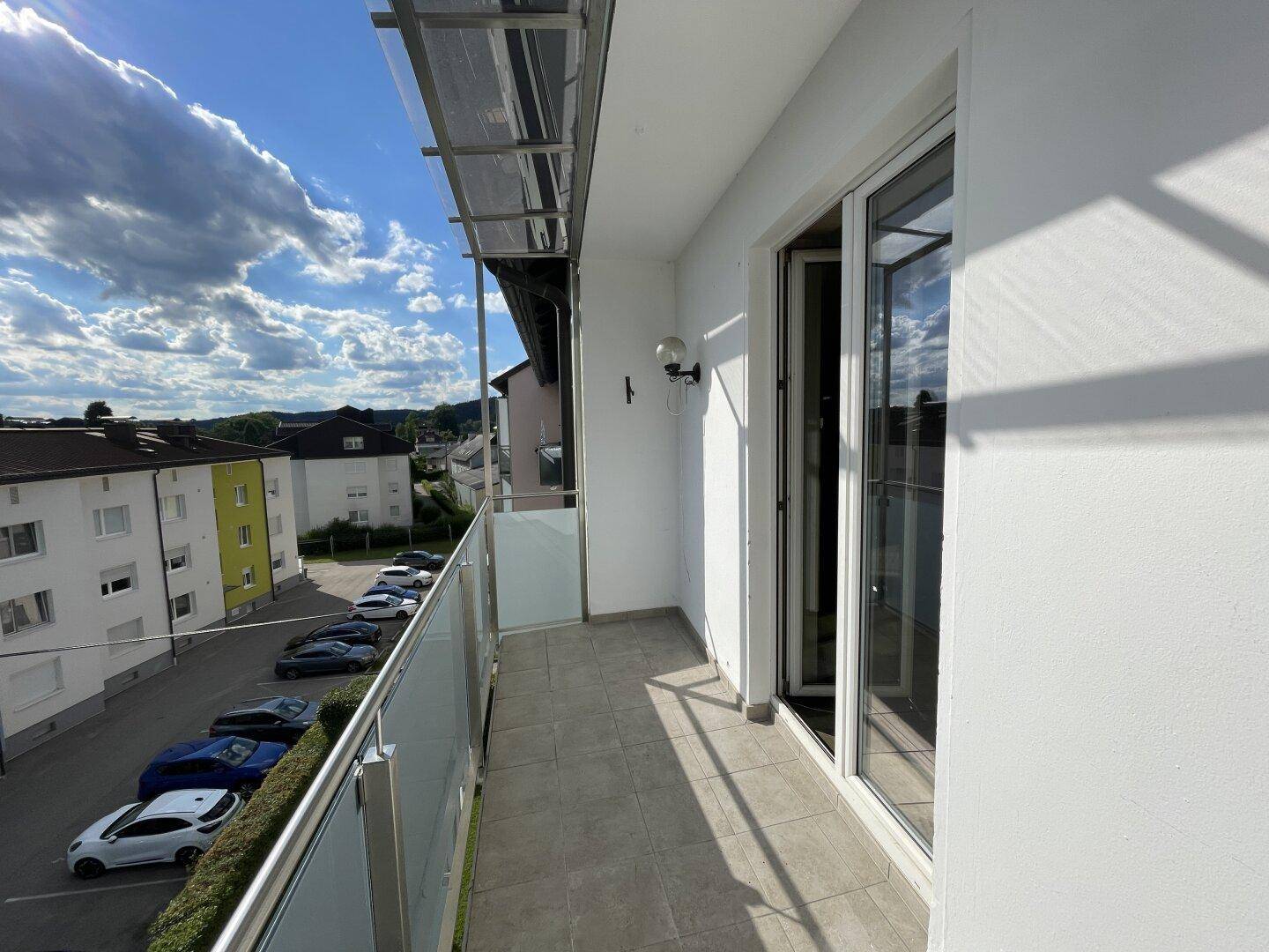 Langer Balkon mit Fliesenboden und Blick auf den Parkplatz und die Gebäude.