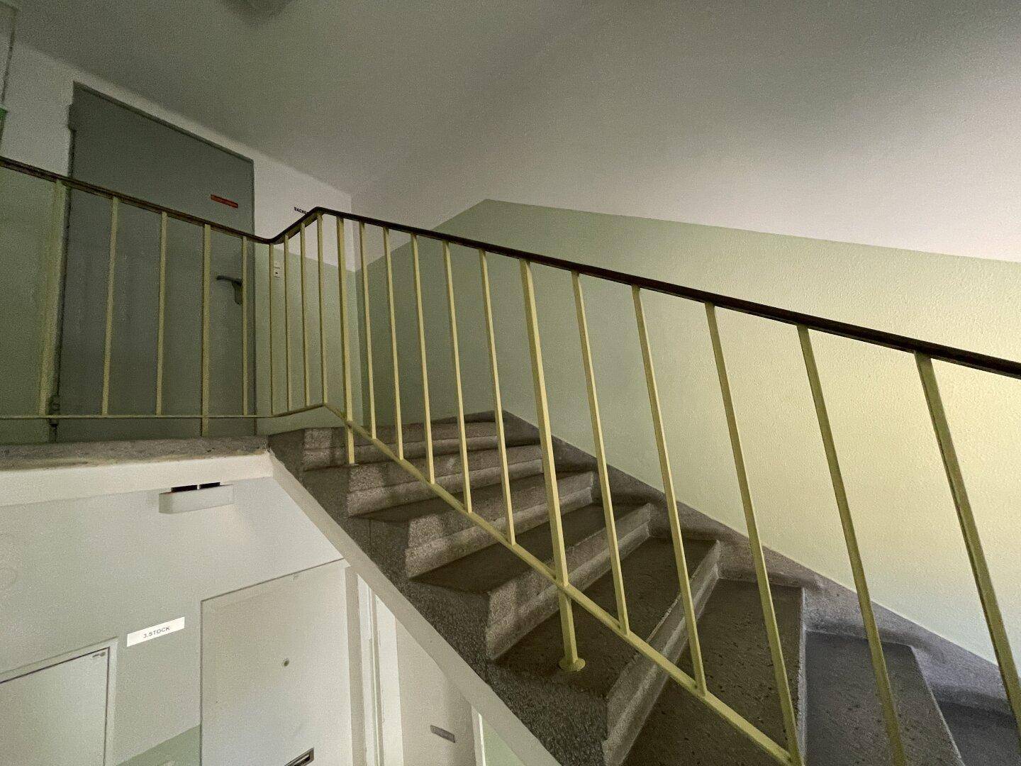 Treppenhaus mit Steinstufen und gelbem Metallgeländer in einem Mehrfamilienhaus.