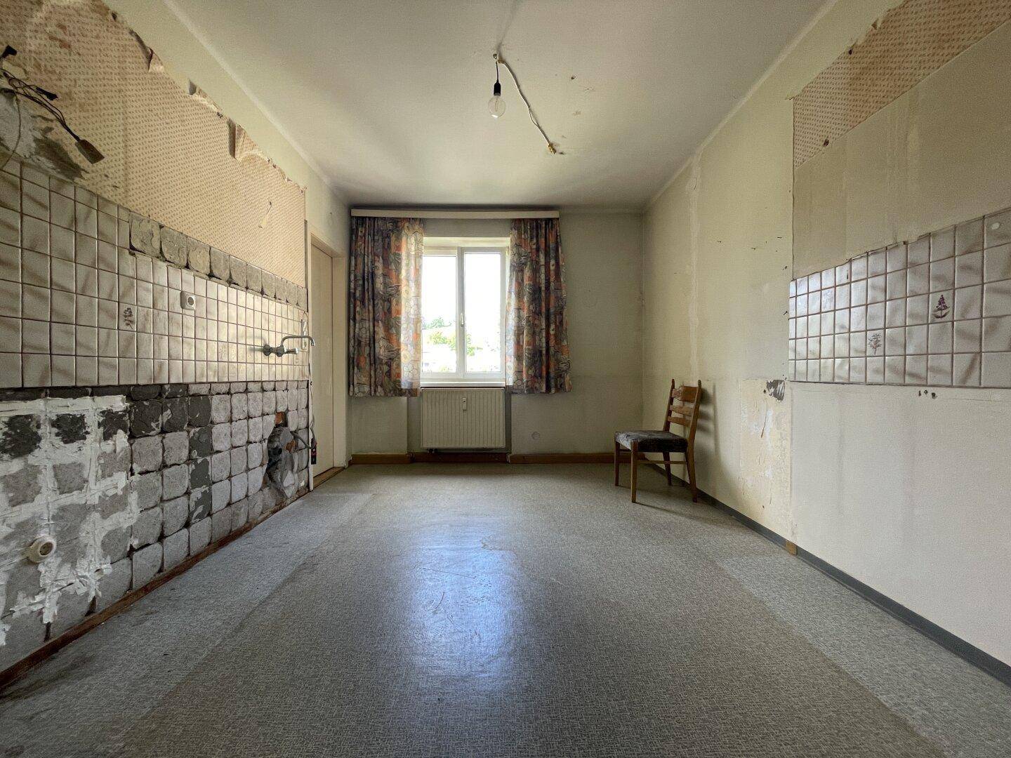 Leere Küche vor der Renovierung mit alten Fliesen und einem Fenster.