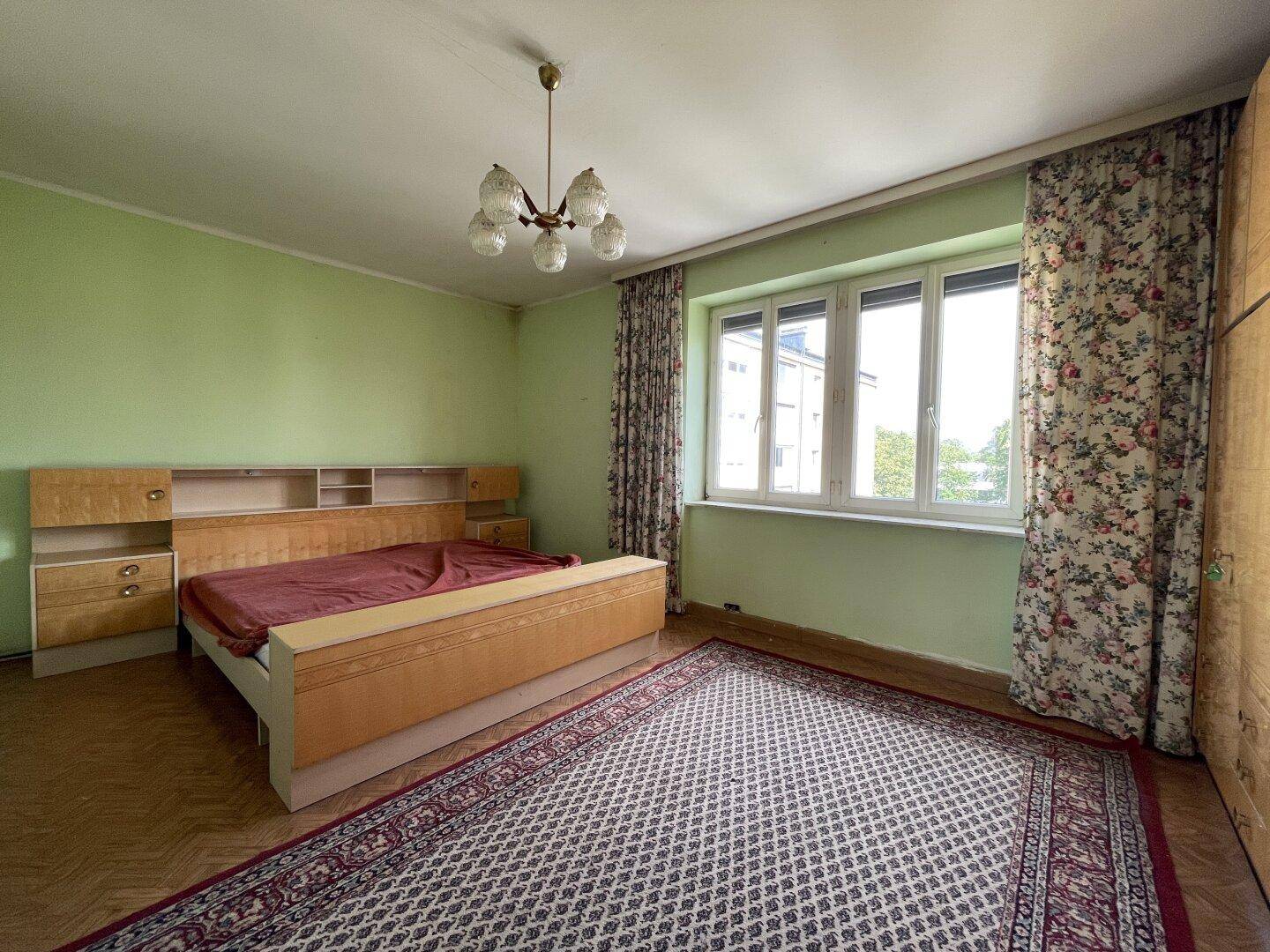 Schlafzimmer mit älterem Bett, grünen Wänden und großem Fenster.