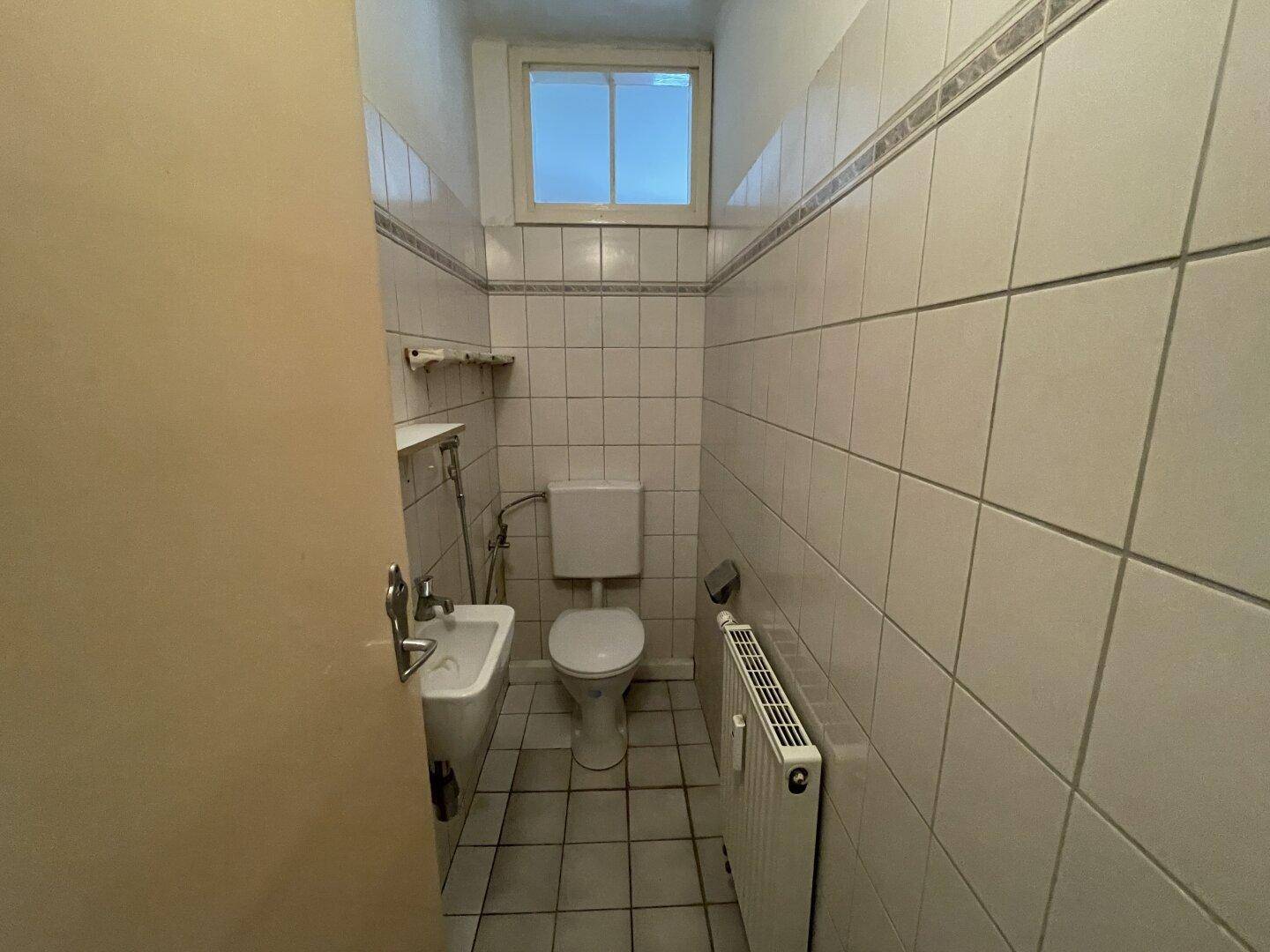 Kleines WC mit Toilette, Waschbecken und Fliesen an den Wänden.
