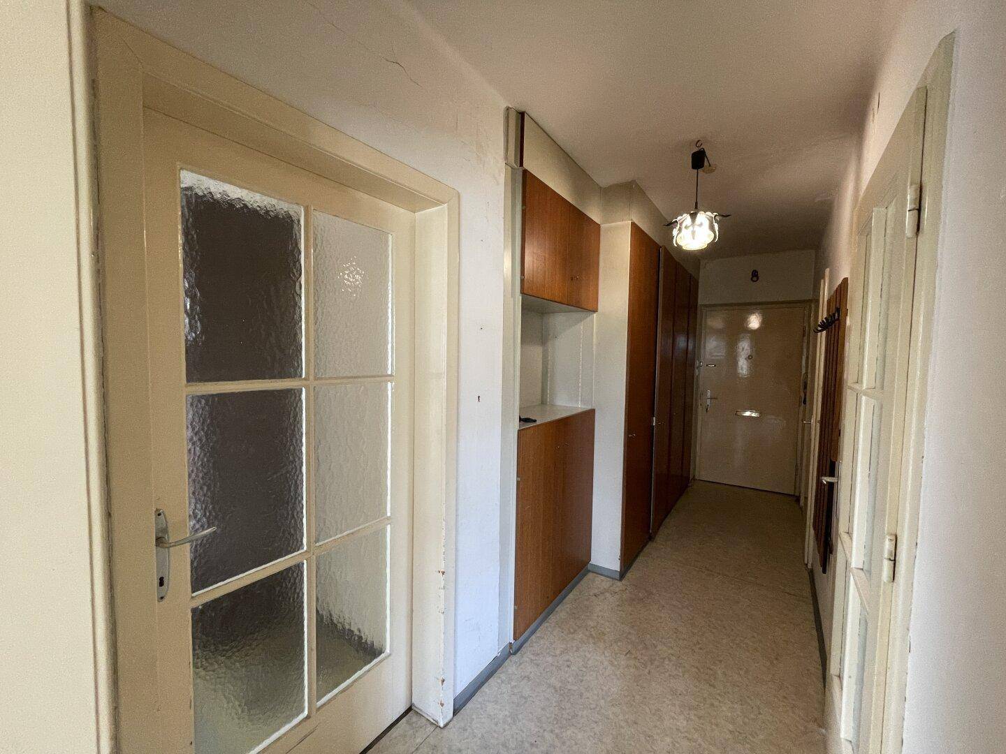 Langer Flur mit älteren Einbauschränken und einer Tür mit Glaseinsatz.