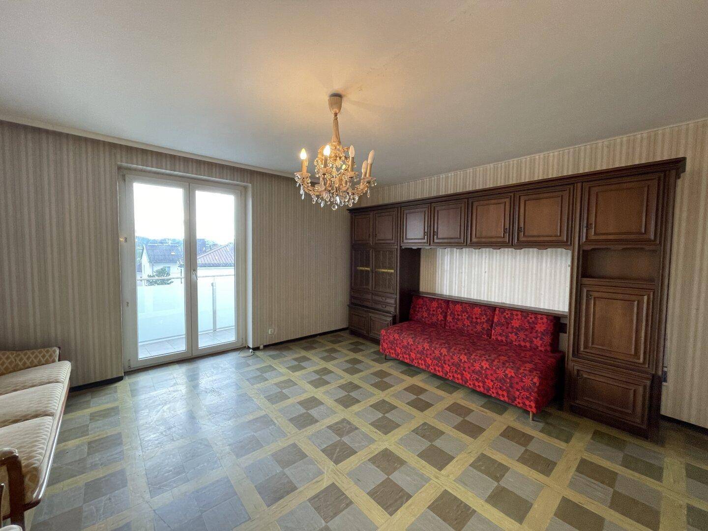 Wohnzimmer mit älteren Möbeln, Kronleuchter und Zugang zum Balkon.