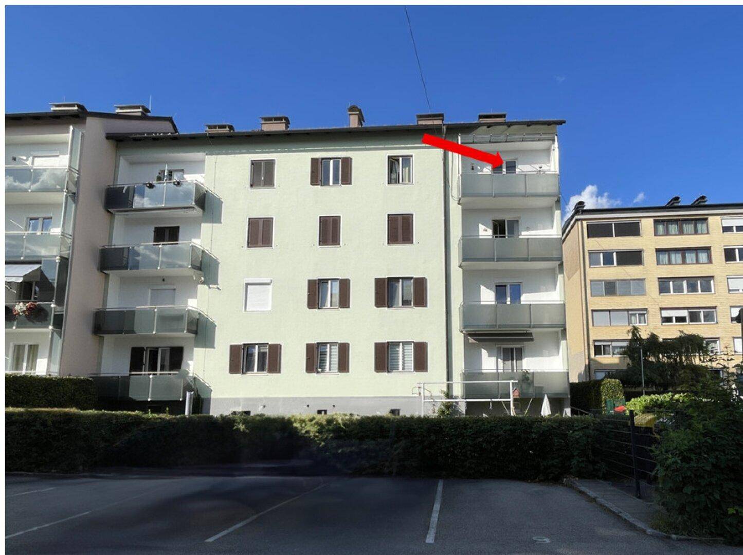 Mehrfamilienhaus mit Balkonen und hellgrüner Fassade unter blauem Himmel.