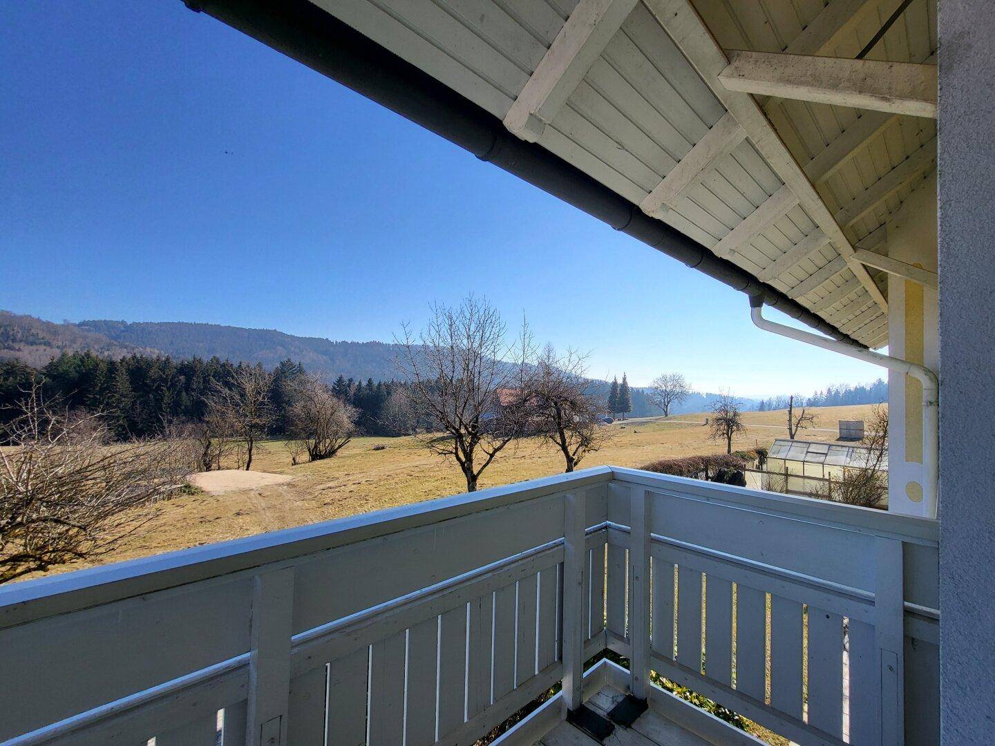 Balkon mit Holzboden und weitem Blick über die ländliche Landschaft und Wälder.