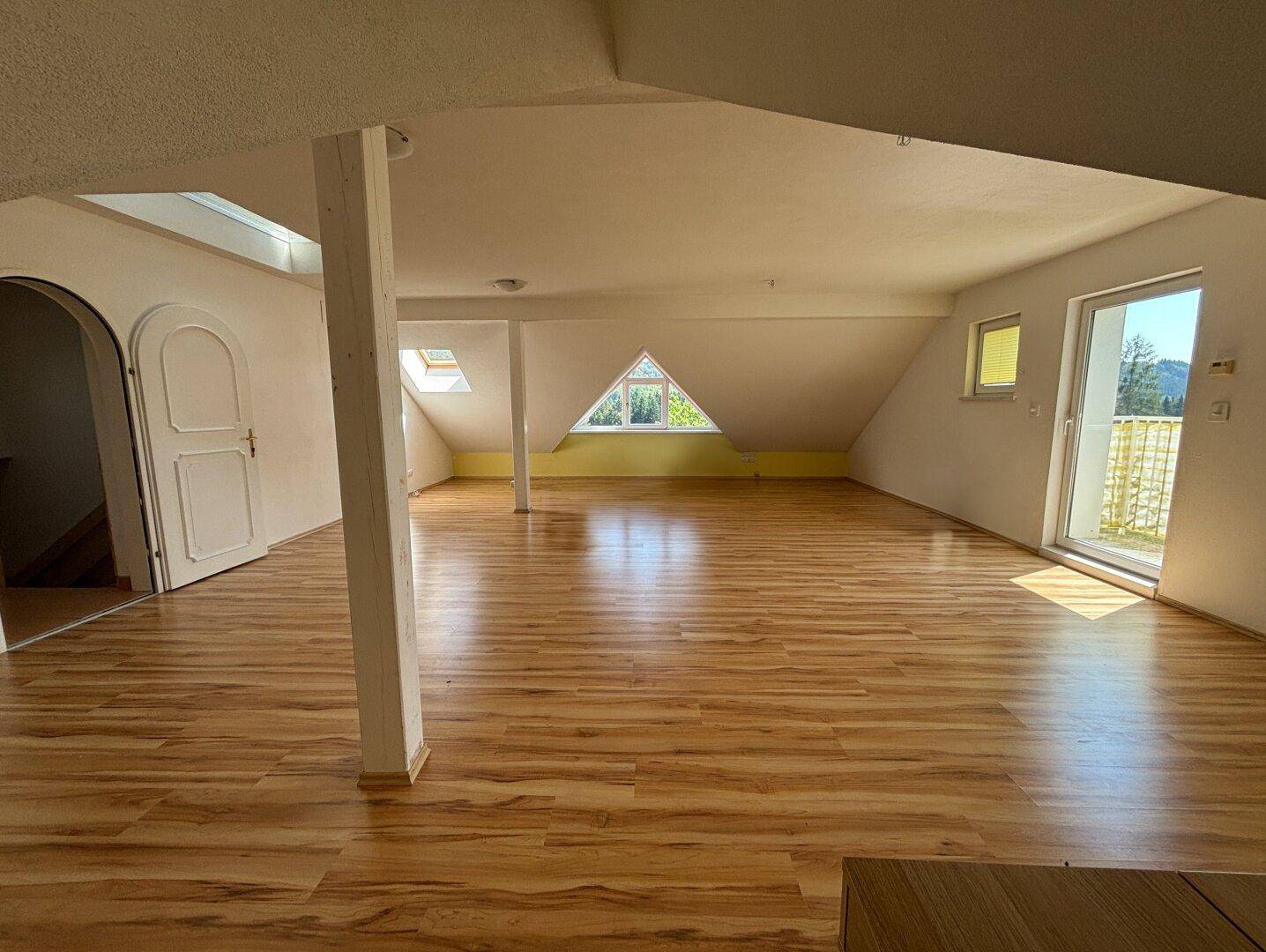 Geräumiger Dachbodenraum mit Holzboden, Dachschrägen und Zugang zu einem Balkon.