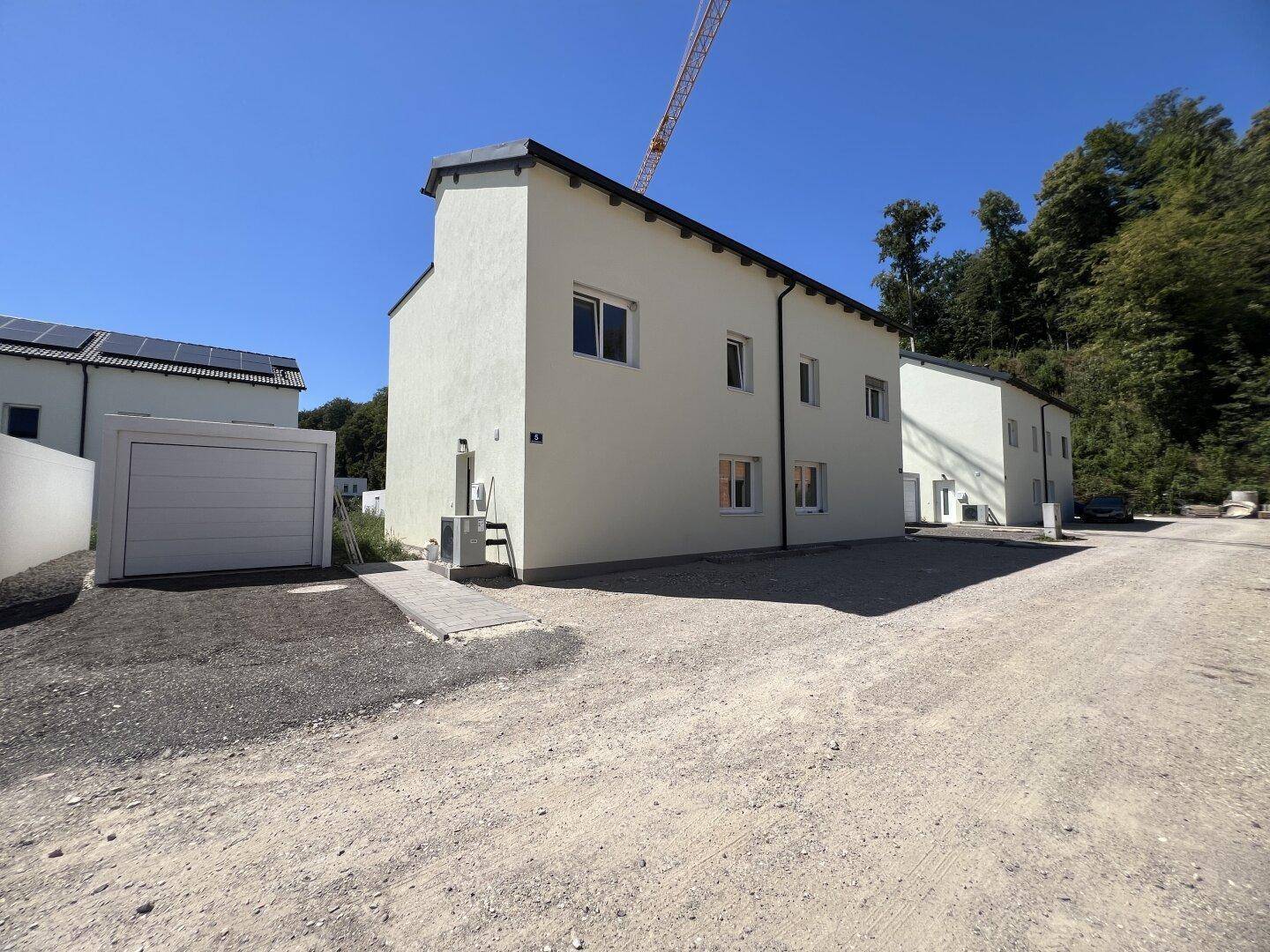 Seitenansicht eines Neubaus mit Garagenzufahrt und angrenzendem Waldgebiet.