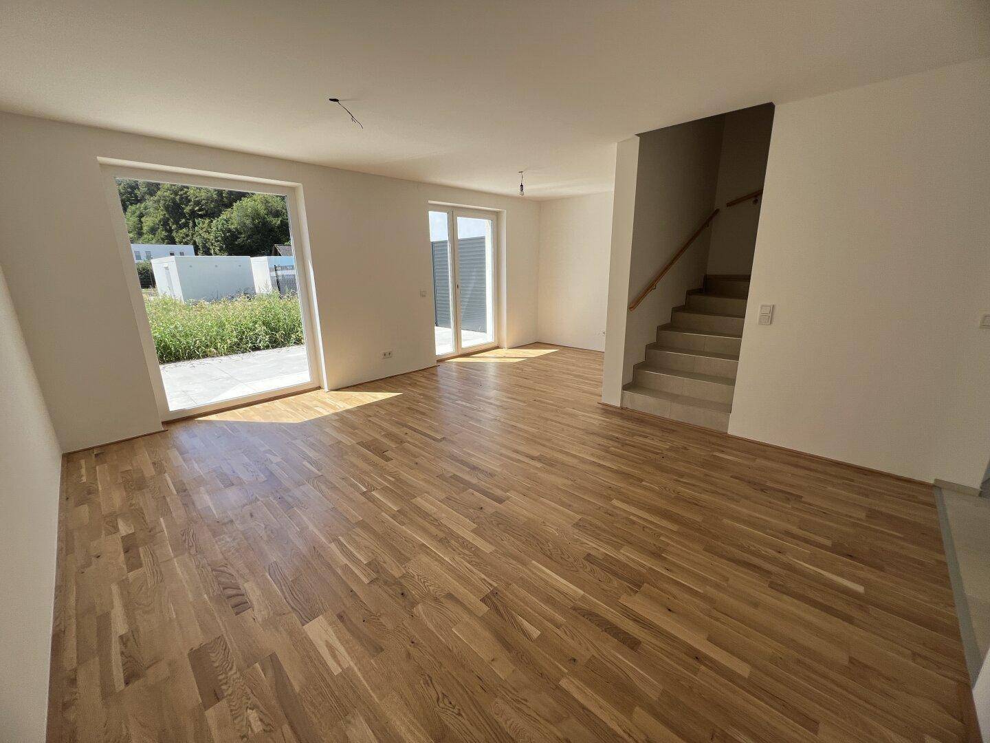 Helles Wohnzimmer in einem Neubau mit neu verlegtem Parkettboden und Zugang zum Garten.
