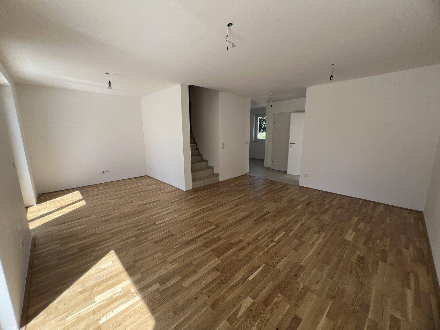 Geräumiges Wohnzimmer mit Holzparkett und offener Treppe zum Obergeschoss.