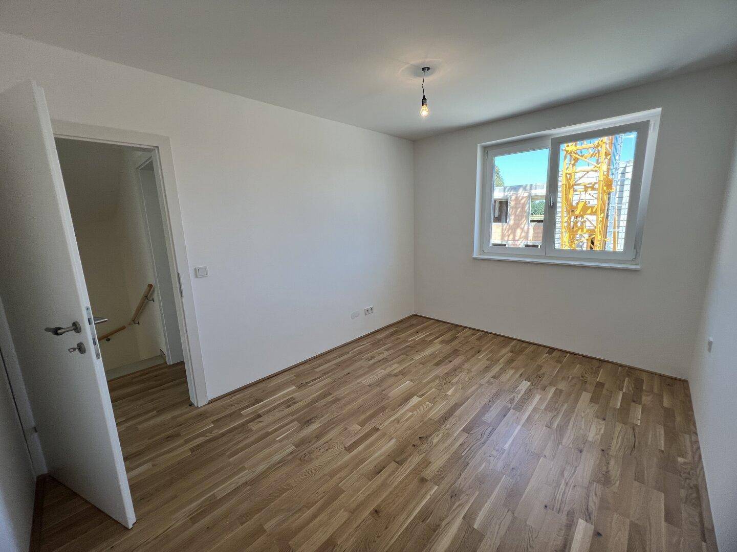 Helles Schlafzimmer mit Parkettboden und Blick auf die Baustelle.