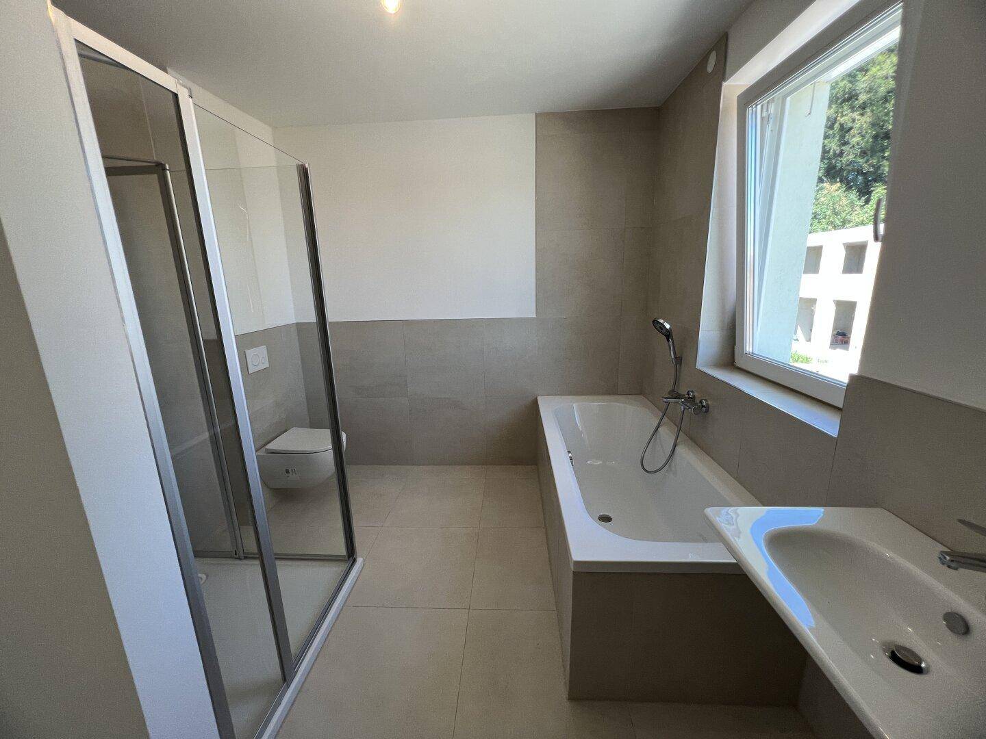 Modernes Badezimmer mit Badewanne, Duschkabine und Fenster für Tageslicht.