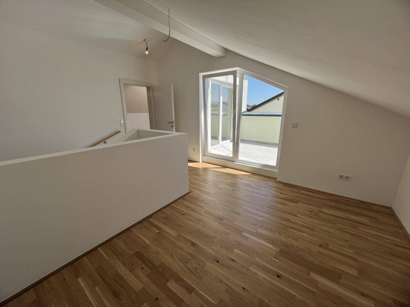 Heller Dachgeschossraum mit Parkettboden und Zugang zu einer Dachterrasse.