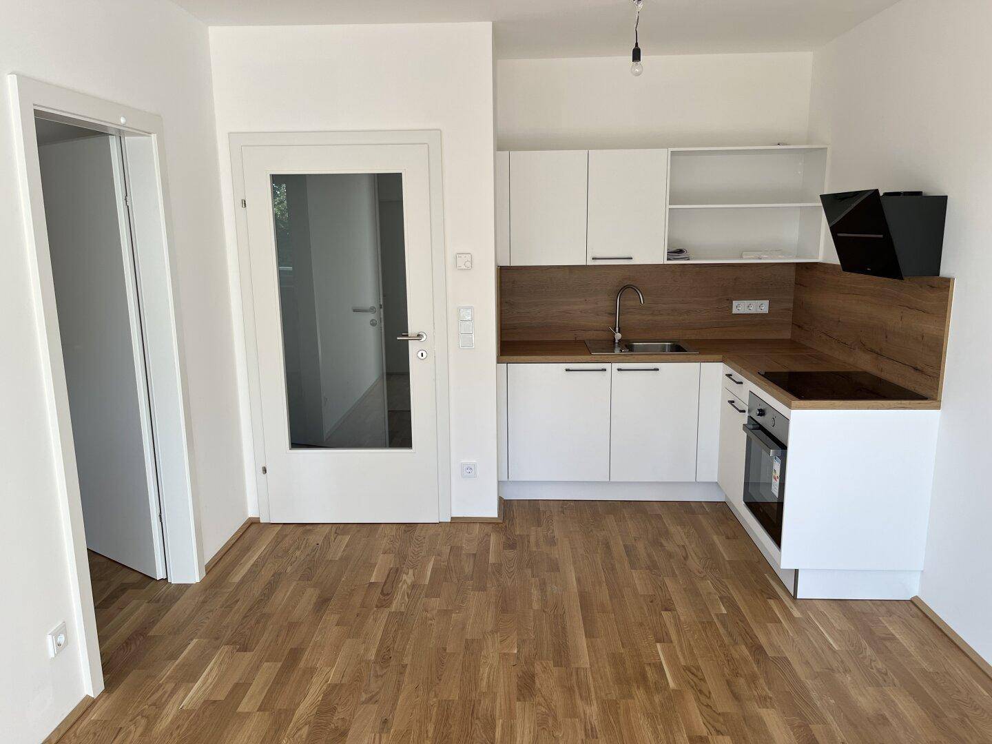 Moderne Einbauküche mit weißen Schränken, Holzarbeitsplatte und Parkettboden.