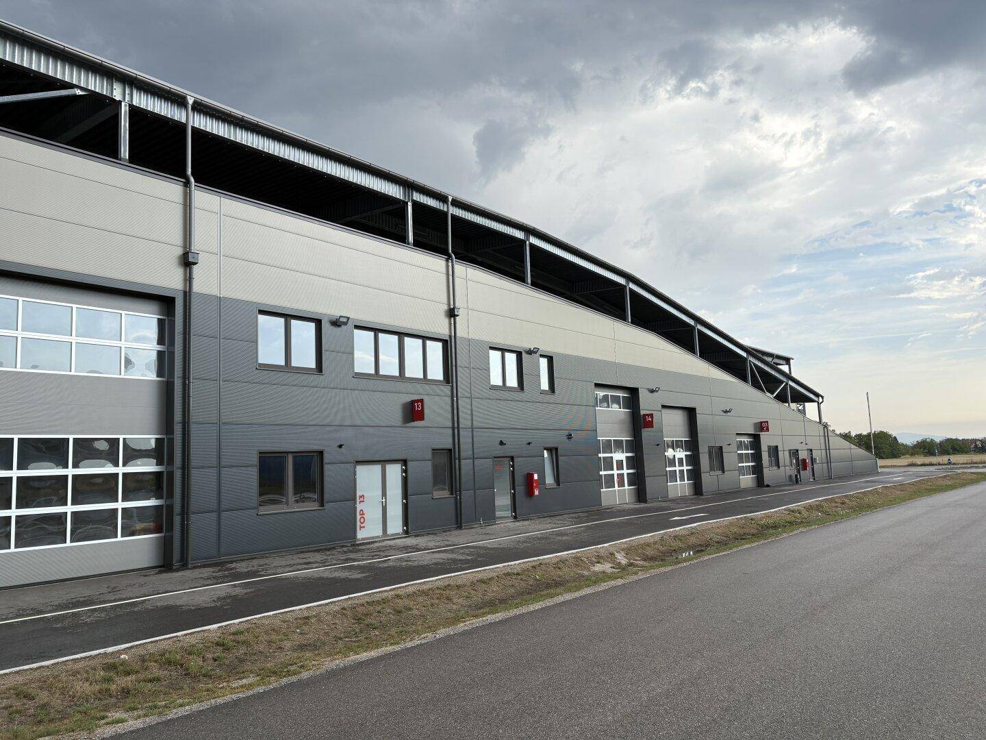 Modernes Industriegebäude mit mehreren Garagentoren und Fenstern unter bewölktem Himmel.