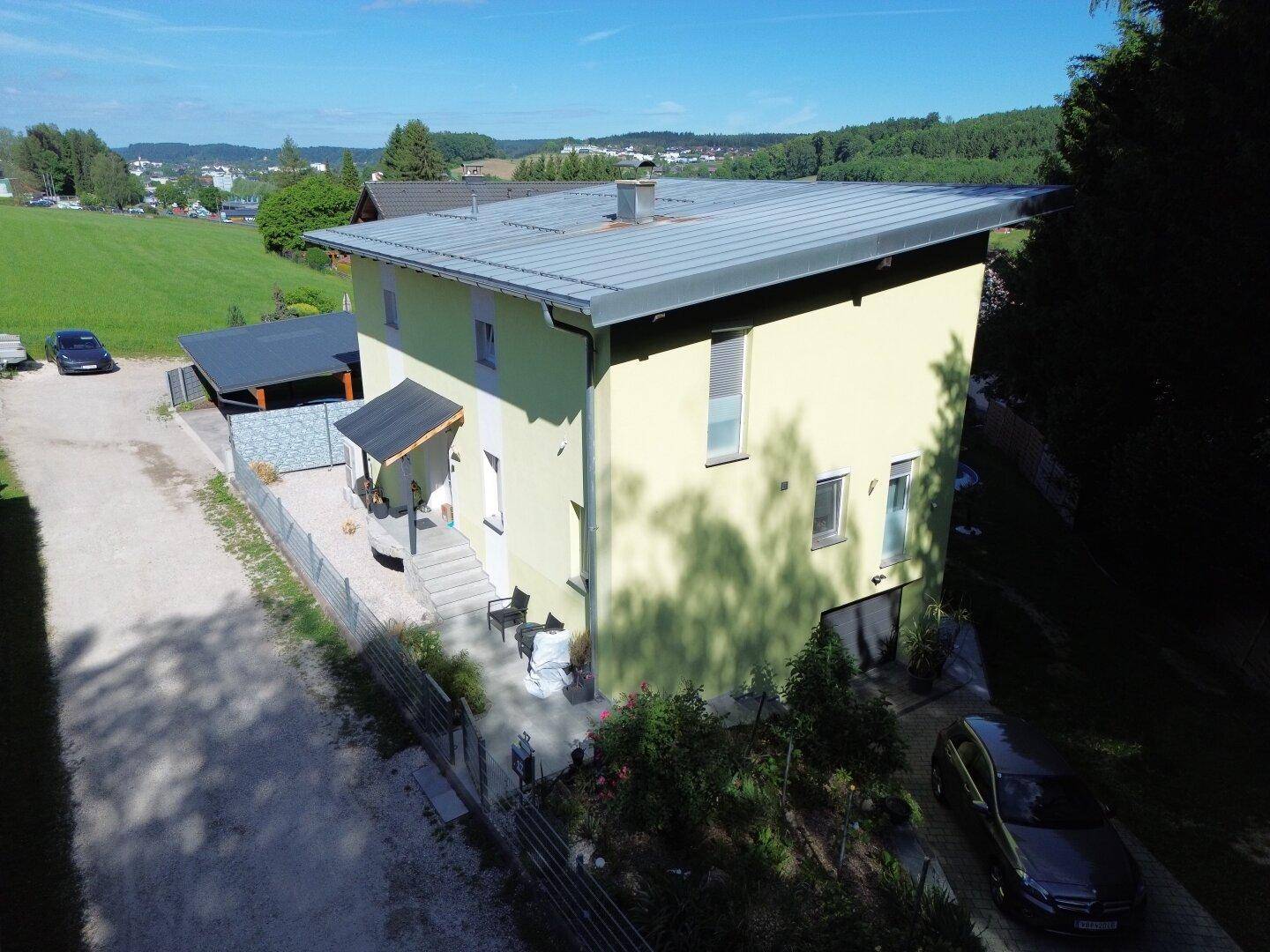 Seitenansicht des Hauses mit gelber Fassade, Flachdach und angrenzendem Feld.