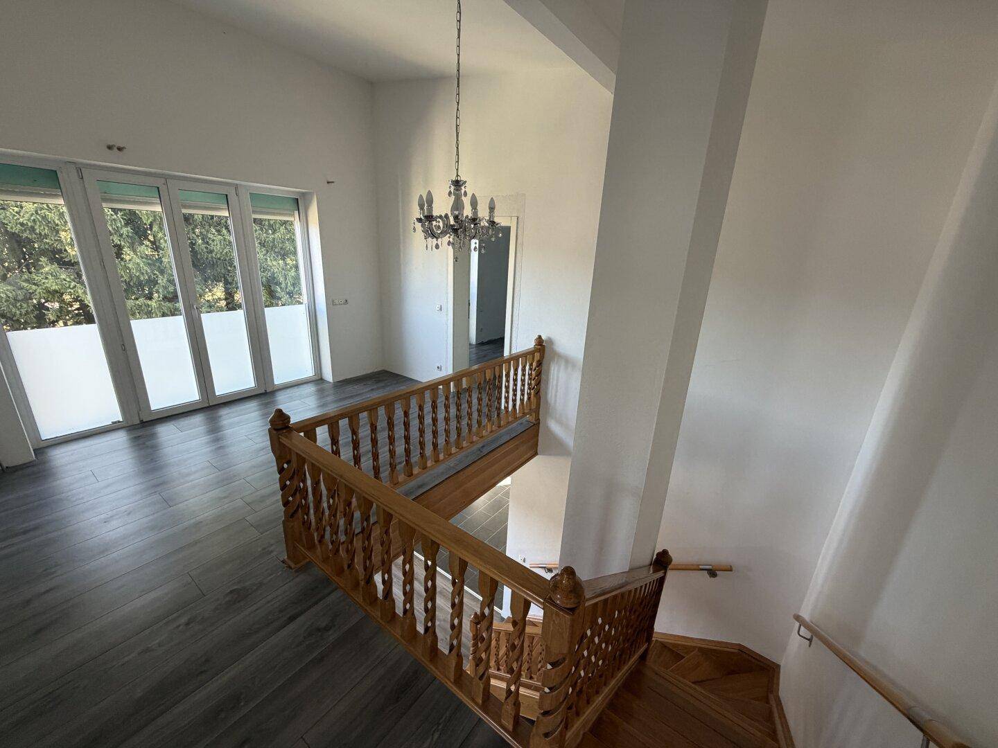 Offener Bereich im Obergeschoss mit Holztreppe, hohen Decken und großen Fenstern.