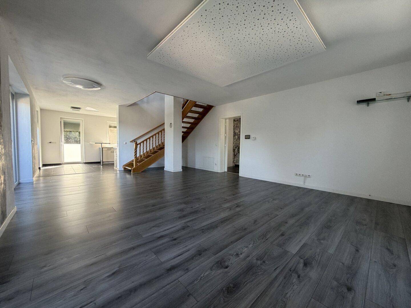 Offener Wohnbereich mit Laminatboden, Treppe und Blick in die angrenzende Küche.