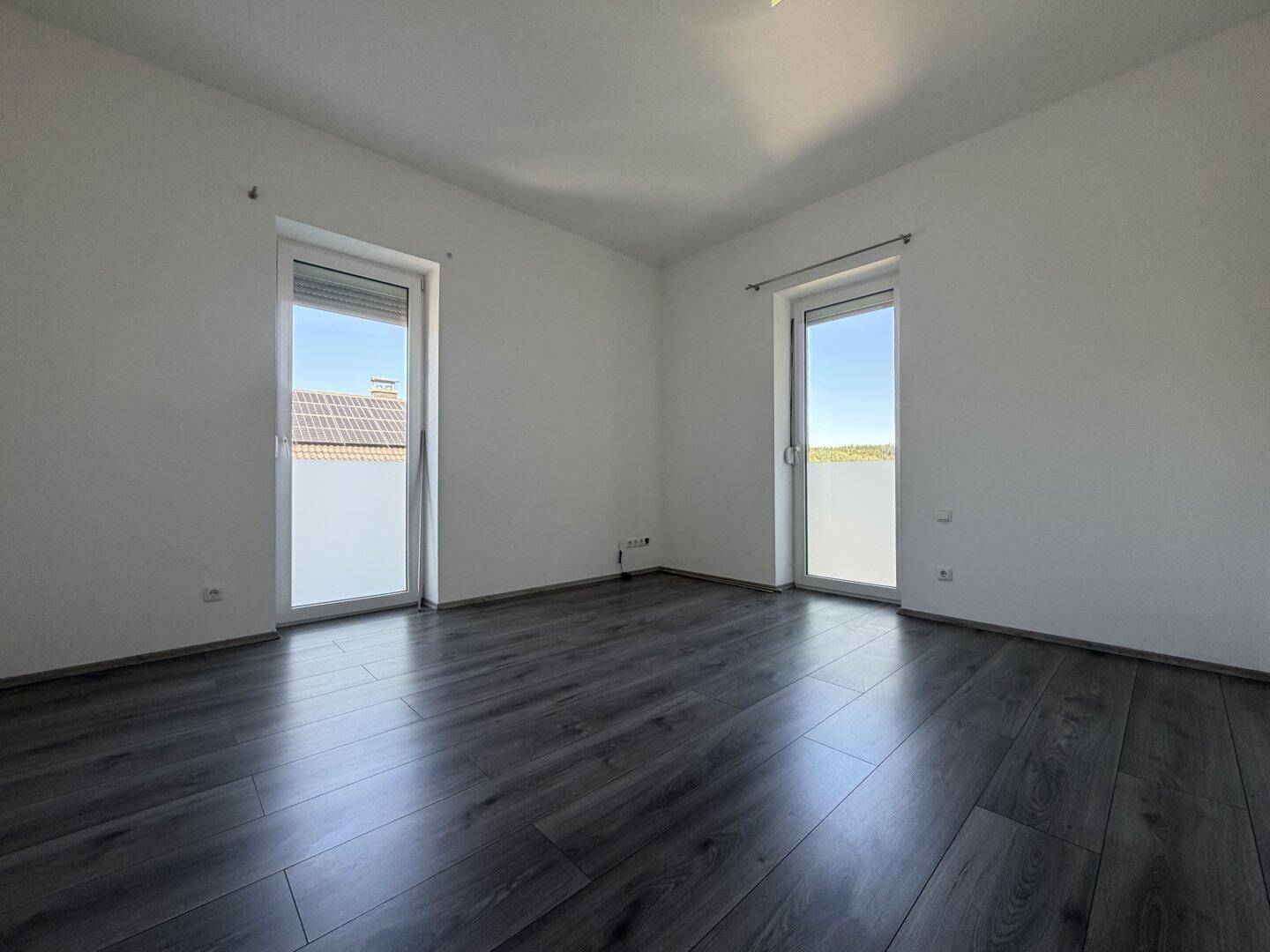 Helles Schlafzimmer mit Laminatboden und zwei Fenstern mit Rollläden.