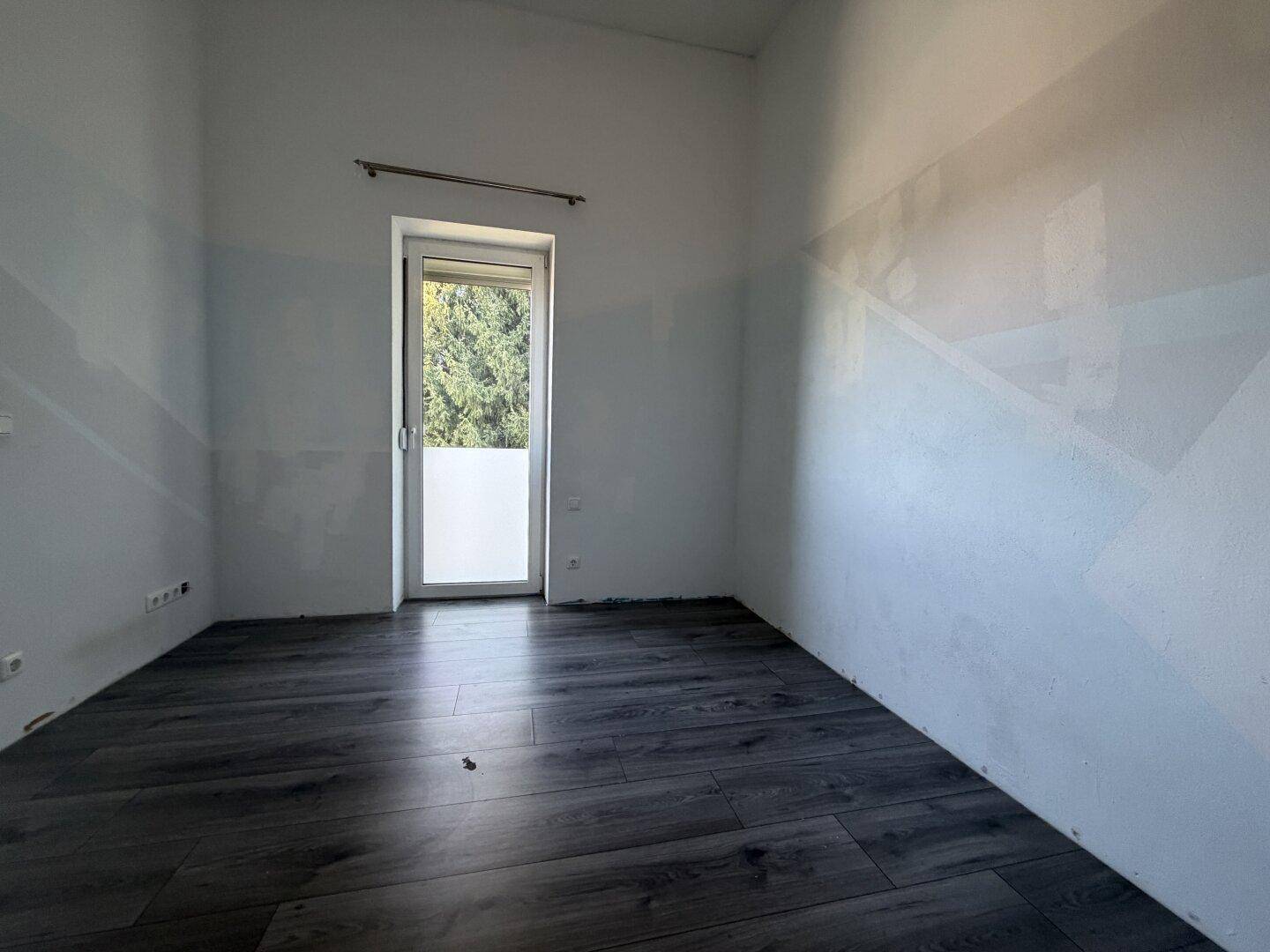 Schlafzimmer mit Laminatboden und einem Fenster mit Blick ins Grüne.