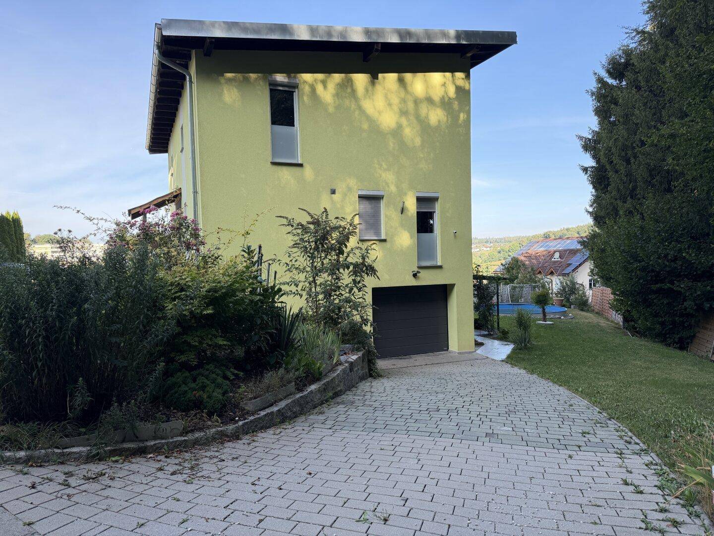 Seitenansicht des Hauses mit Garage, gepflasterter Auffahrt und Gartenbereich.