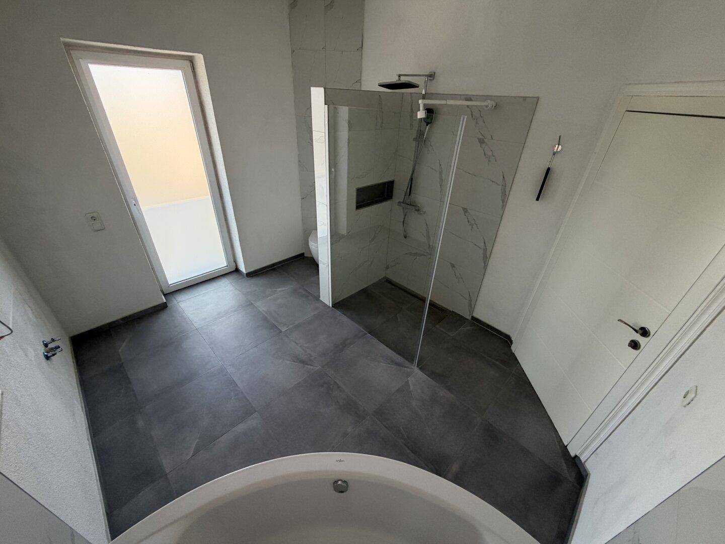 Modernes Badezimmer mit Dusche, Badewanne und dunklen Fliesen.