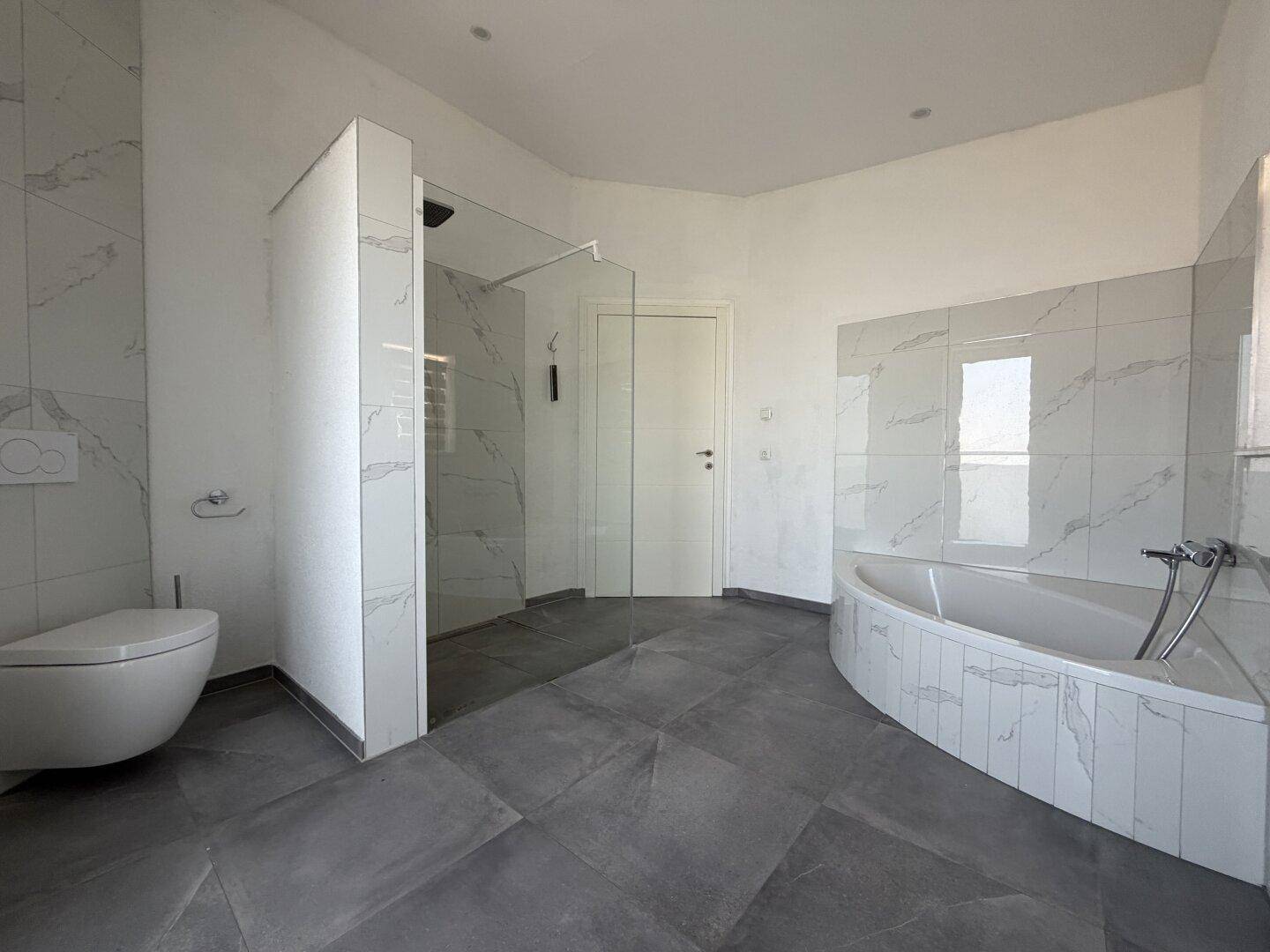 Großes Badezimmer mit freistehender Dusche, Badewanne und modernen Fliesen.
