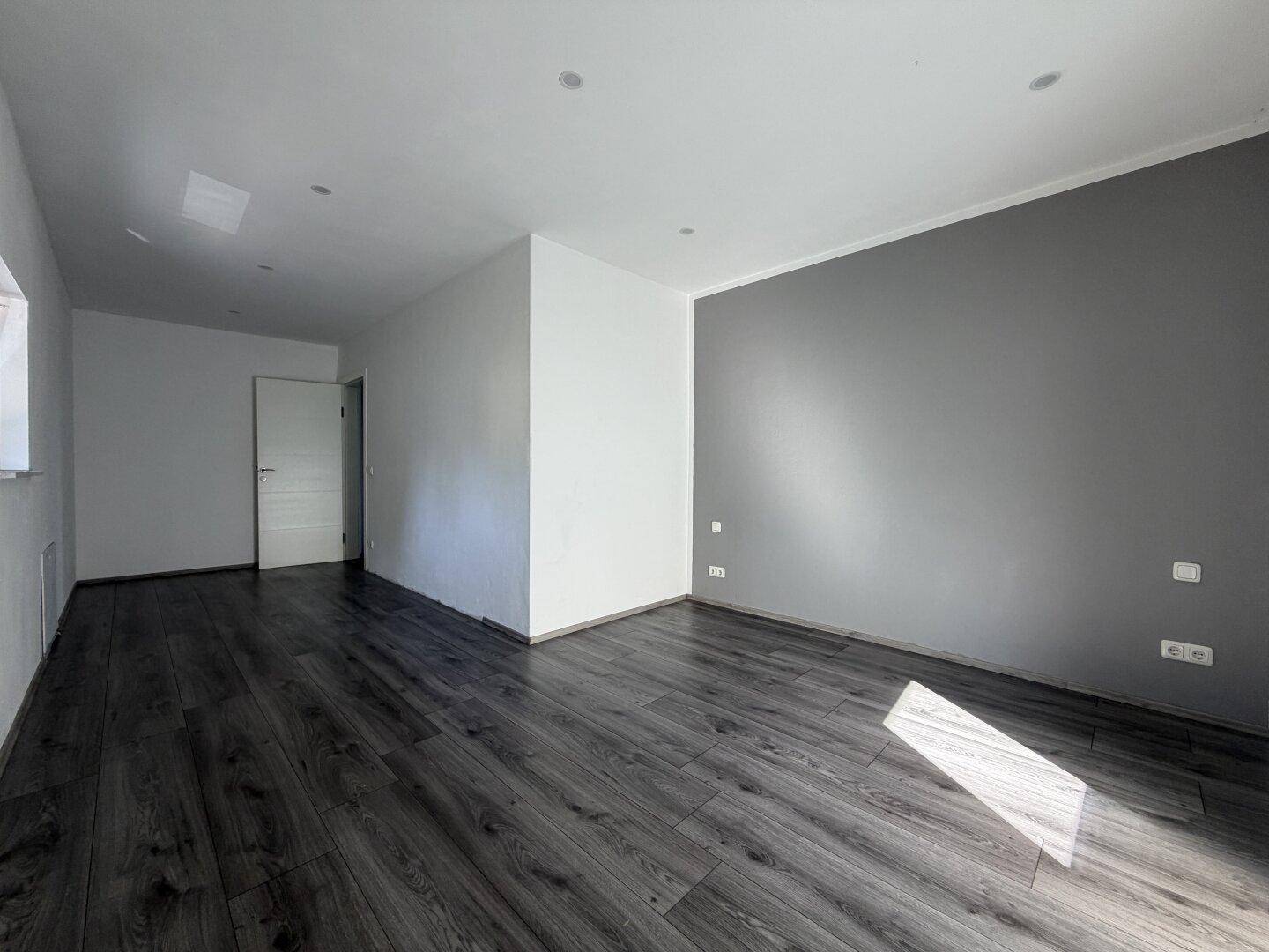 Geräumiger Raum mit dunklem Laminatboden und einer grauen Akzentwand.