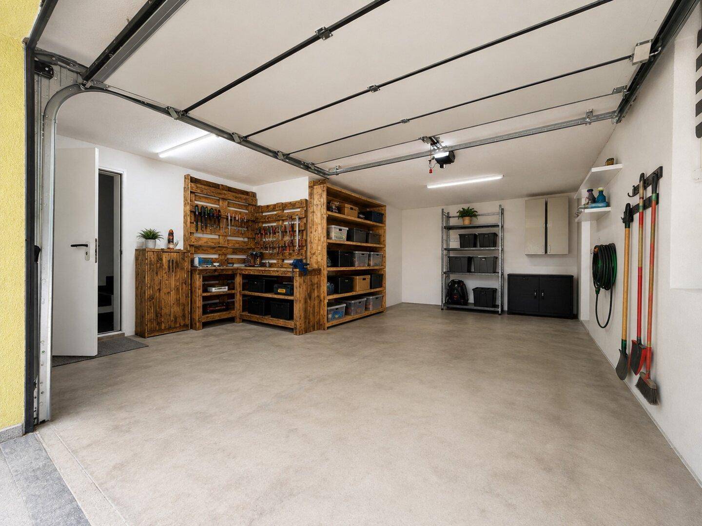 Geräumige Garage mit Werkstattbereich, Regalen und Rolltor.