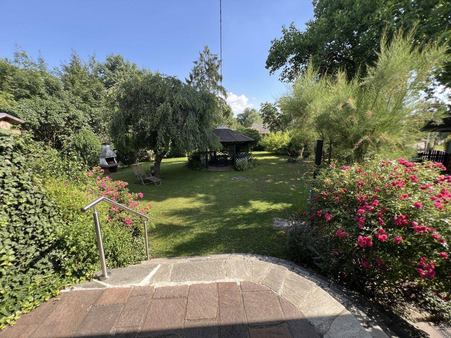 Weitläufiger Garten mit Pavillon, Grillplatz und vielfältiger Bepflanzung, ideal für Entspannung im Freien.